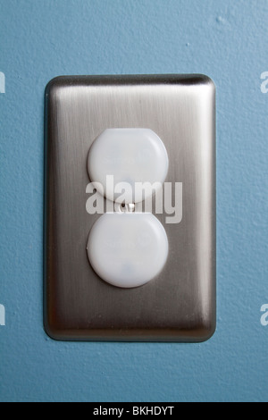 A North American electrical outlet with safety plugs and a stainless steel plate on a blue wall. Stock Photo
