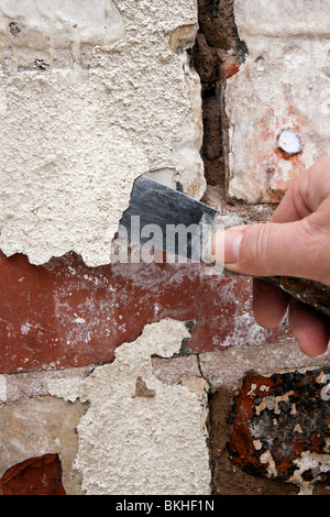 house maintenance man scraping off flaking paint on old brickwork in need of repointing & painting Stock Photo