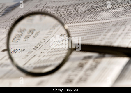 Magnifying glass highlighting stock quotes in business section of newspaper. Stock Photo