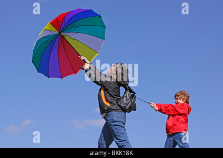 young boy holding on to his mother who is being blown away by the wind Stock Photo