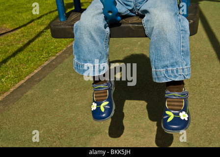 Child's legs hanging down from child's playground swing Stock Photo