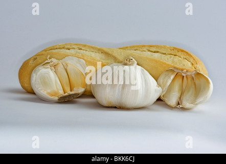 Loaf of bread behind whole garlic head and cloves of garlic on a plain white background Stock Photo