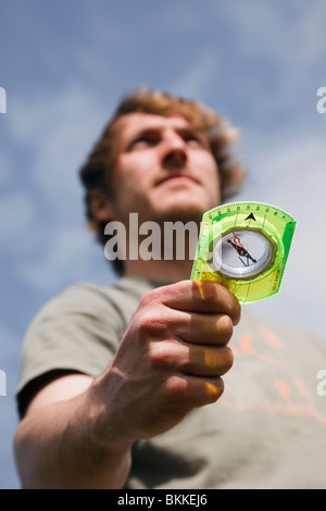 Young millennial man hiker using an orienteering compass in hand to point in right direction to go ahead looking to a positive future. England UK Stock Photo