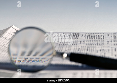 Magnifying glass highlighting stock quotes in business section of newspaper. Stock Photo