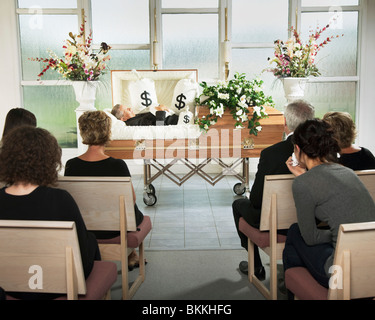 The Deceased Laying In A Coffin At His Funeral With Bags Of Money Surrounding Him Stock Photo