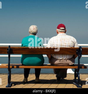 Rear view of an elderly senior couple man woman sitting on seaside bench, summer afternoon, UK Stock Photo
