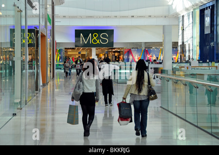 Back view women shoppers walk shopping mall with Marks and Spencer retail business store in Westfield indoor shopping mall Shepherds Bush England UK Stock Photo