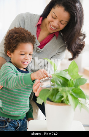Mixed race mother helping son water plants Stock Photo