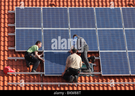 Workmen installing solar panels on a roof Stock Photo