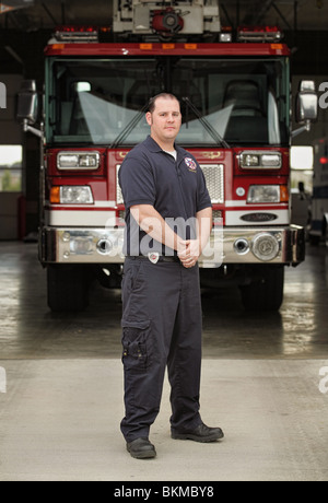 full-length fireman standing in front of fire engine at firehouse wearing blue uniform Stock Photo