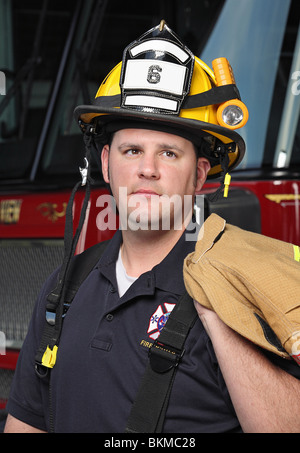 handsome young fireman wearing helmet in front of fire truck looking away Stock Photo