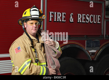 handsome young fireman holding fire hose in uniform in front of firetruck Stock Photo
