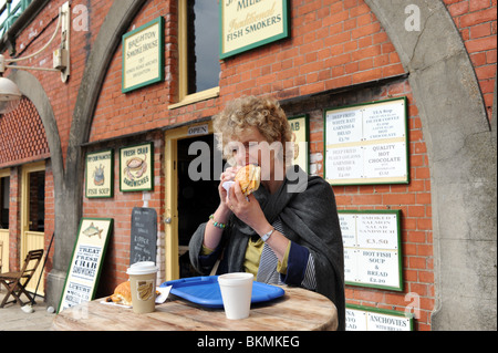 Woman eating fresh grilled kipper in a roll at Brighton Smokehouse on the seafront UK Stock Photo