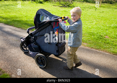 Baby being pushed in a pram / push chair being pushed by a small boy, aged five years old. Stock Photo