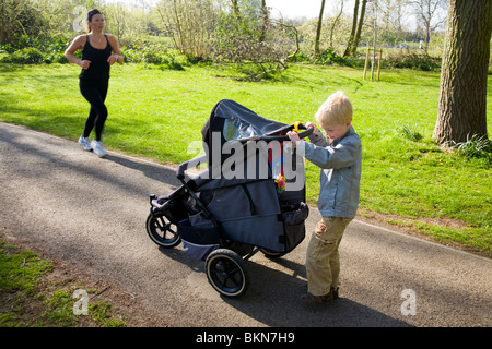 Baby being pushed in a pram / push chair being pushed by a small boy, aged five years old. Stock Photo