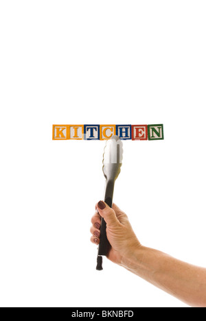 Woman with tongs holding children's blocks that spell 'KITCHEN' Stock Photo