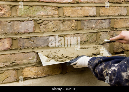 A brick wall being re-pointed / builder pointing a wall with a pointing trowel. Stock Photo