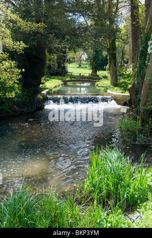 The river Glyme at Glympton, Oxfordshire, with a footbridge and small waterfall / weir, spring sunshine, Stock Photo