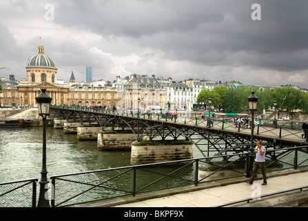 Pedestrians walking on Pont des Arts bridge and view of Institut de France in Paris, France under a stormy sky. Stock Photo
