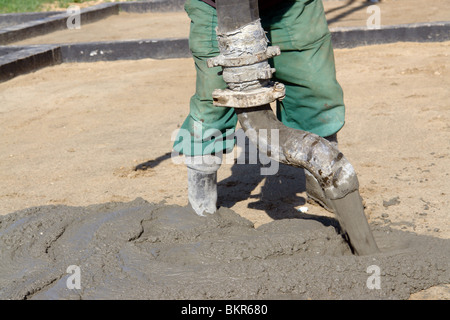 Closeup of construction worker pouring concrete mix from pump onto compacted foundation surface Stock Photo