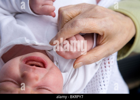 Close up of an older woman's hand holding the hand of a newborn / new born baby. Stock Photo