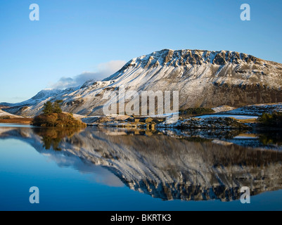 A winter view of Cregennen Lakes in late afternoon sun with a snow covered crags in the background reflected in the lake Stock Photo