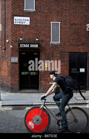 Covent Garden, West End, London. Bike passing the rear stage door entrance to the Cambridge Theatre on Shelton Street Stock Photo