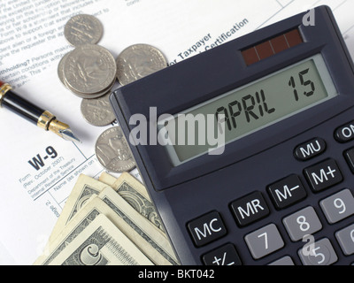 Calculator with lcd displaying April 15 placed on W-9 income tax forms with pen, and American dollars Stock Photo