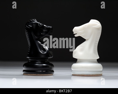 Black and white chess knights standing face to face over black background Stock Photo