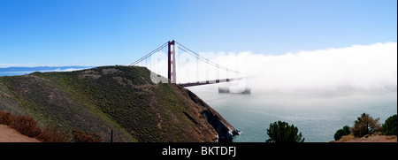 SAN FRANCISCO, California - Panoramic shot of Golden Gate Bridge on a sunny day partially obscured by fog with a ship heading out to sea
