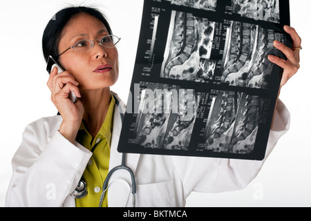 Asian female doctor looking at an MRI scan while talking on a cellphone. Horizontal shot. Isolated on white. Stock Photo