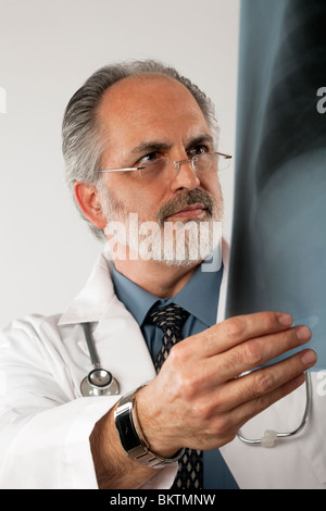 Portrait of a doctor wearing eyeglasses and a white lab coat and looking intently at an x-ray. Vertical shot. Isolated on white. Stock Photo