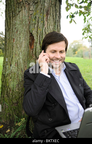 Man sitting under a tree with telephone and computer Stock Photo