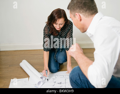 Two colleagues looking at blueprints on floor Stock Photo