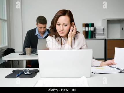 Woman looking at laptop, colleague working in background Stock Photo