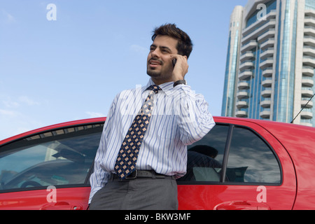 Businessman standing by car and using mobile phone Stock Photo