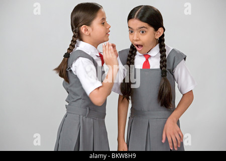 Two girls wearing school uniform telling secrets to each other Stock Photo