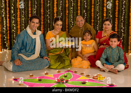 Three generation Indian family in front of rangoli, young woman holding a plate of sweets Stock Photo