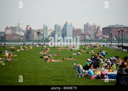 People take advantage of the warm weather on the lawn of a pier in Hoboken, New Jersey Stock Photo