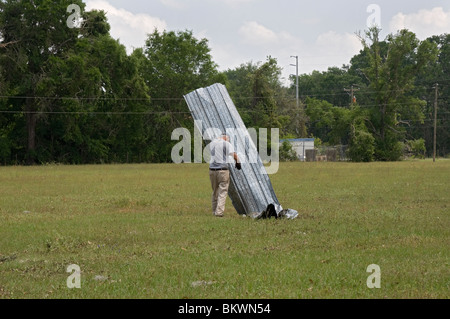 man moving parts of barn tossed into pasture land after tornado touched down during storm near Branford Florida Stock Photo