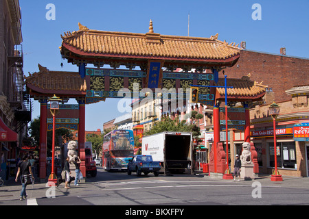 Colourful gate to entrance of Chinatown with marble lions at the base and locals crossing the street in Victoria Stock Photo