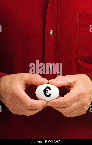Man holds white egg with the Euro sign (€) written on it, symbolizing the fragility of money matters; the proverbial 'nest egg.' Stock Photo