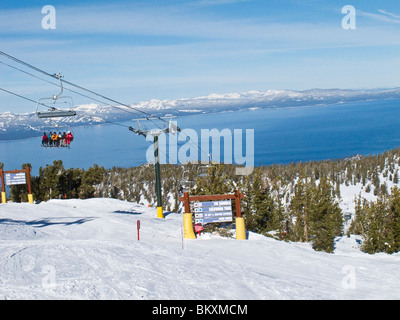 Skiers on ski lift from partway up the ski slope at Heavenly Mountain Resort in winter.Lake Tahoe is in background. Stock Photo