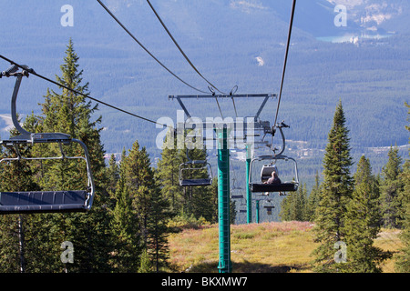 Traveling downwards on the Lake Louise Gondola with fir and pine trees covering the hillside and Lake Louise in the distance Stock Photo