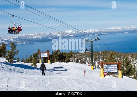 Skiers on ski lift from partway up the ski slope at Heavenly Mountain Resort in winter.Lake Tahoe is in background. Stock Photo