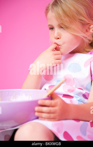 Close up of a young girl holding a baking bowl sucking her finger