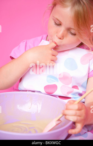 Close up of a young girl holding a baking bowl sucking her finger