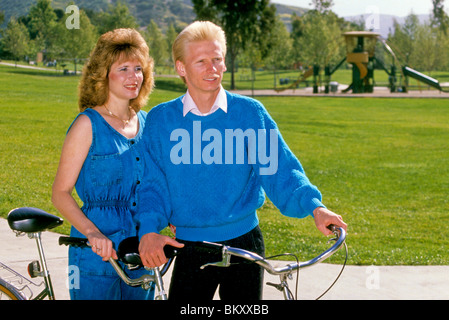 Young blond couple rest while riding bicycle built for two tandem bike in park Stock Photo