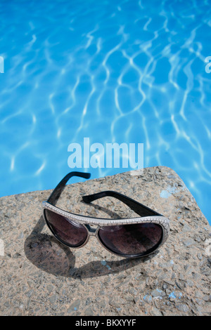 Sunglasses resting on the edge of a blue swimming pool