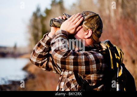 Young man in a camouflage hat wearing a backpack using binoculars, Florence, Montana. Stock Photo